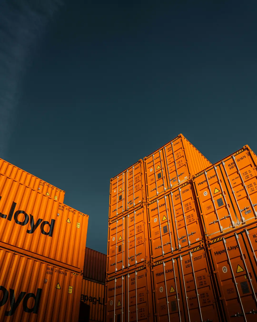 Gestapelte orange Schiffscontainer vor blauem Himmel.